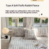 A light gray rabbit fleece blanket and pillows displayed on a bed, with natural light coming through the window.