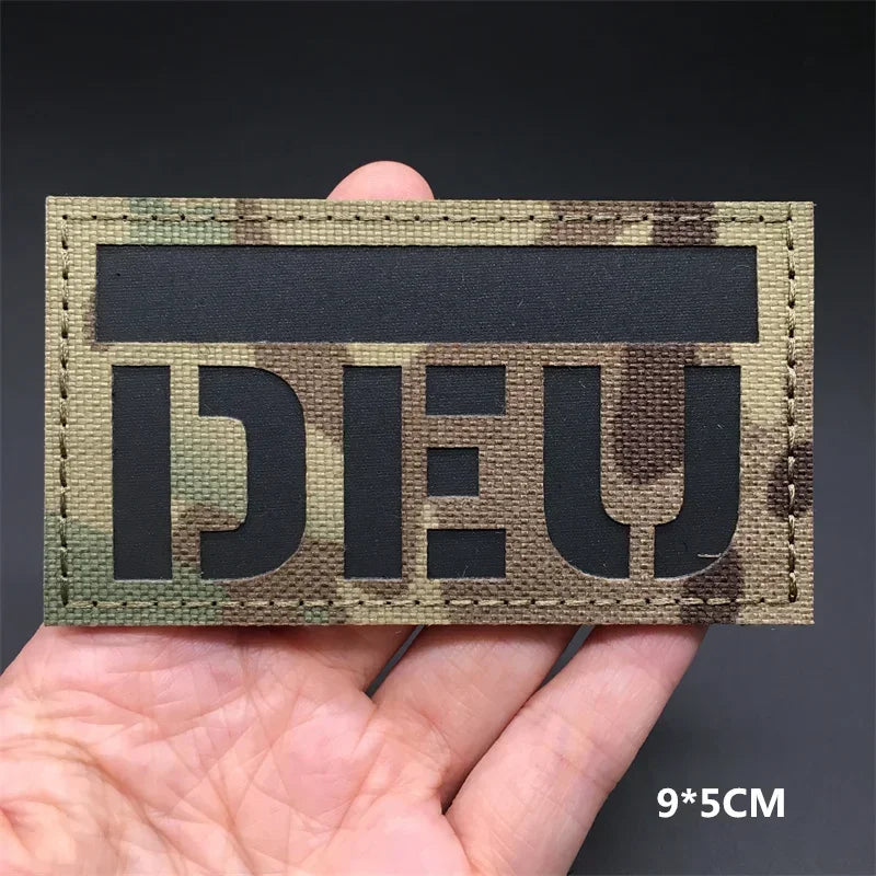 A dark camouflage tactical patch featuring the German flag design with hook-and-loop backing.