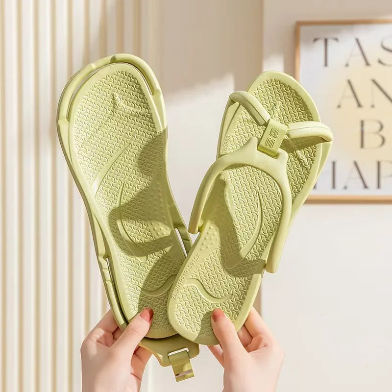 A pair of light green foldable EVA travel slippers being held by hands against a light background.