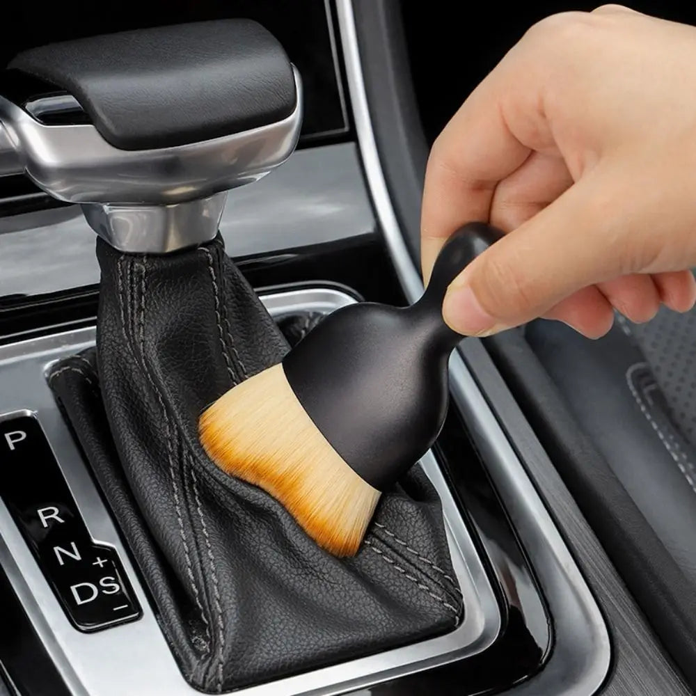 A hand is using an ultra-soft curved detailing brush with a wooden handle to clean car vents or gaps.