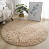 A fluffy beige shaggy round rug placed on a light wooden floor next to a sofa and a framed green leaf artwork.