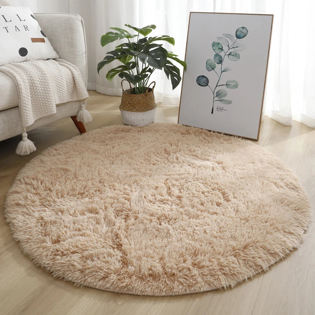 A fluffy beige shaggy round rug placed on a light wooden floor next to a sofa and a framed green leaf artwork.