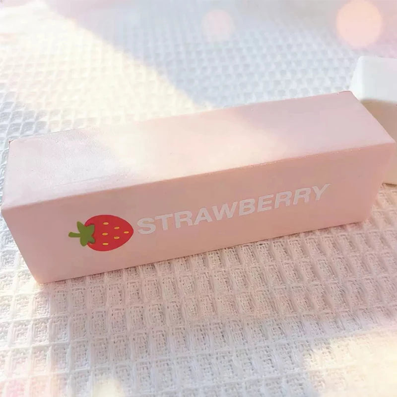 A pink butter fidget stick with a strawberry design resting on a white textured surface.