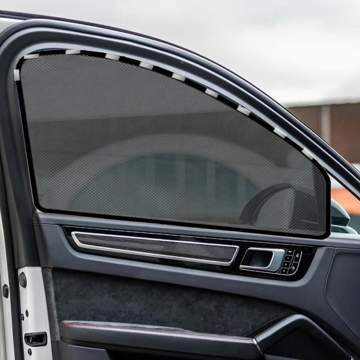 Close-up of a car window featuring a dark mesh sunshade and a silver trim panel.