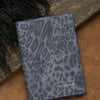 A dark blue leopard print passport holder with personalized name embossing resting on a brown surface.