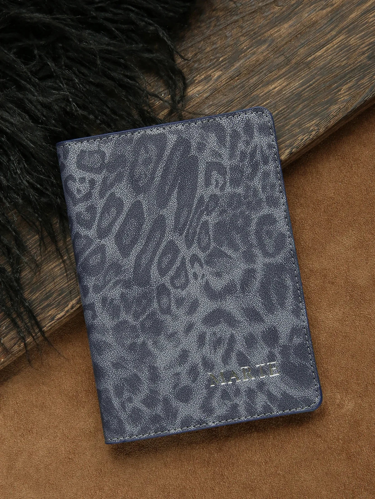 A dark blue leopard print passport holder with personalized name embossing resting on a brown surface.