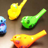 Three bright plastic bird whistles in yellow, green, and orange are displayed on a dark surface.
