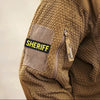 Close-up of a brown sherpa fleece sleeve featuring a yellow sheriff patch with hook and loop backing.