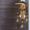 A rustic witch bells door hanger wind chime with brass bells and wooden accents hanging on a dark brown door.