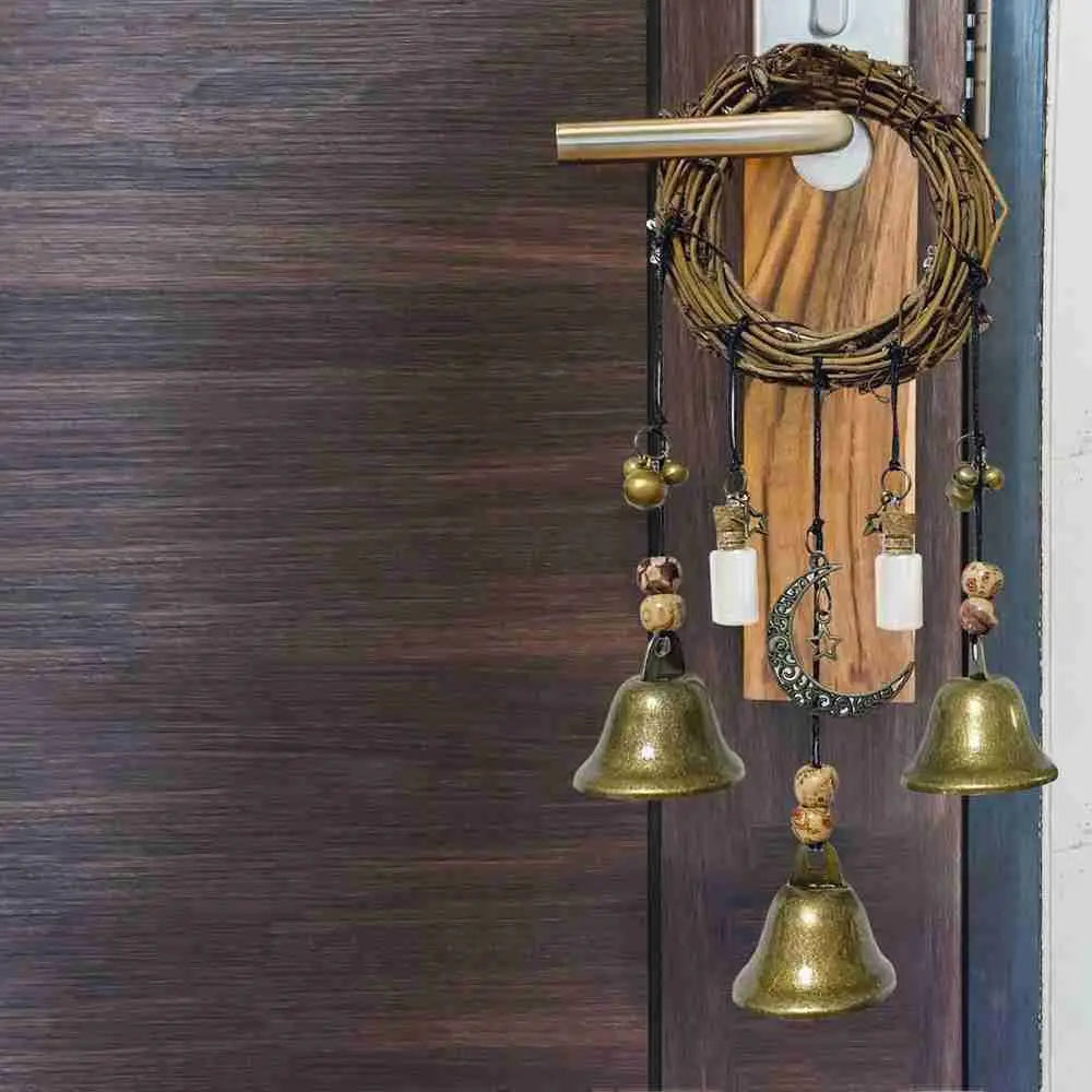 A rustic witch bells door hanger wind chime with brass bells and wooden accents hanging on a dark brown door.