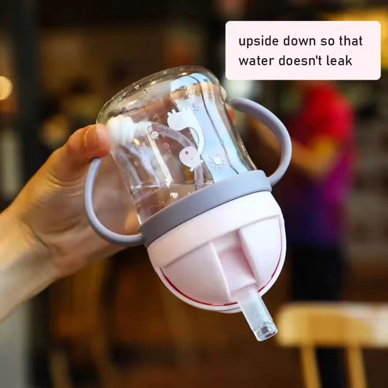 A hand holds a clear plastic straw cup with handles upside down to prevent leakage.