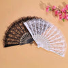 A pair of vintage lace folding hand fans, one black and one white, displayed on a beige background.