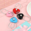 Three heart-shaped combination padlocks in red, pink, and black on white cord against a light pink background.