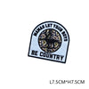Black and white embroidered patch with text NAMAS LET YOUR BOYS BE COUNTRY surrounding a circular hunting motif