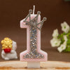 A pink number candle shaped like the numeral one decorated with silver rhinestones and a crown.