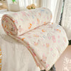 A rolled and unfolded cream-colored quilt with a floral print featuring pink, orange, and yellow animals on a white bed.