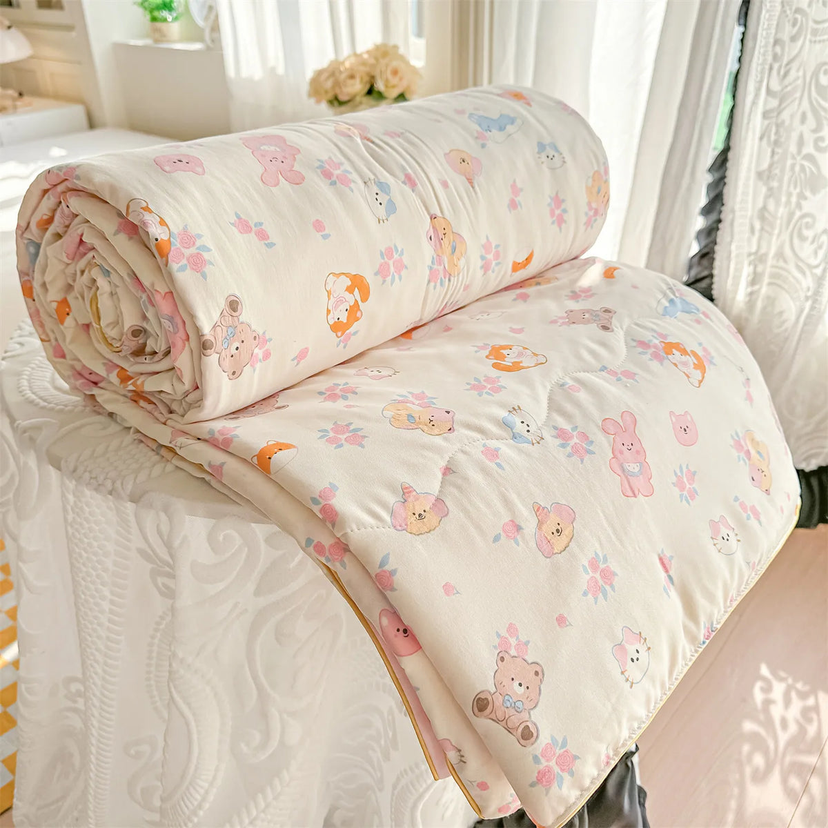 A rolled and unfolded cream-colored quilt with a floral print featuring pink, orange, and yellow animals on a white bed.