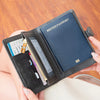 A hand holds an open black passport wallet featuring RFID protection and multiple card slots.