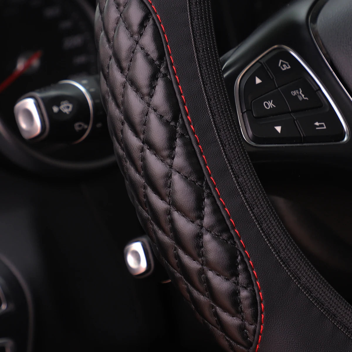 Close-up of a black quilted steering wheel cover with red stitching and controls visible.