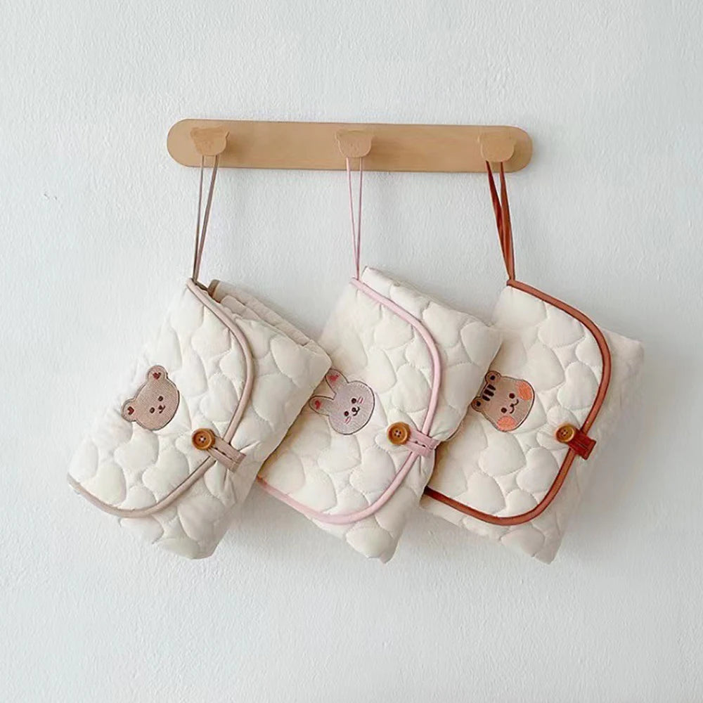 A white quilted foldable portable diaper changing pad is hanging on a wooden rack.