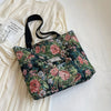 A floral patterned corduroy tote bag resting on a white fabric next to a piece of paper.