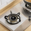 A black reusable gas stove burner protector with a central burner ring is placed on a stainless steel surface.