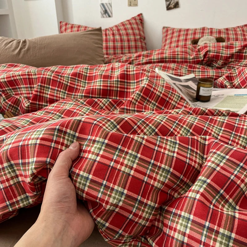 A hand touches a red and green plaid duvet cover set featuring a tartan pattern.