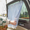 A hand holds a blue and white checkered sun shade curtain inside a car window.
