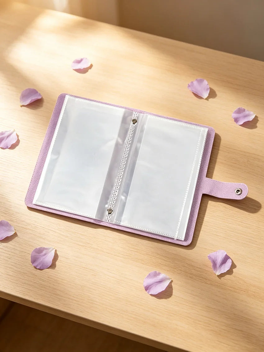 A lilac organizer binder with transparent pages is displayed on a wooden surface surrounded by pink flower petals.
