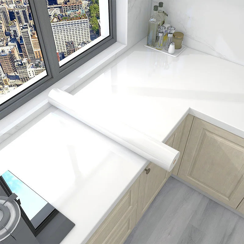Roll of white marble peel-and-stick wallpaper displayed on a kitchen countertop next to a window view.