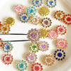 A collection of multicolor sew-on flower rhinestones in various shades of pink, blue, and gold are displayed on a white surfa