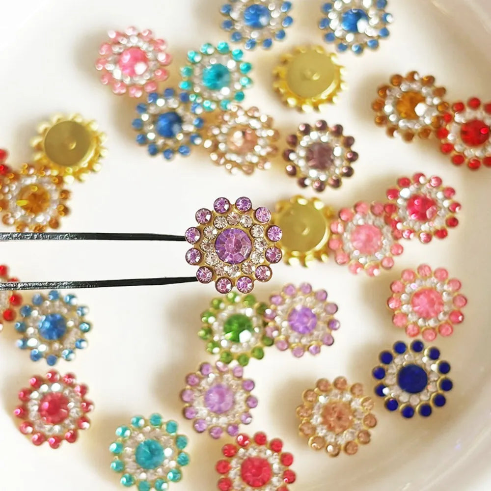 A collection of multicolor sew-on flower rhinestones in various shades of pink, blue, and gold are displayed on a white surfa