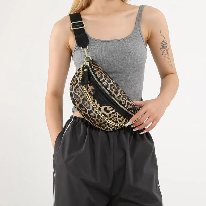 A woman is holding a leopard print waist bag with a black strap and gold hardware, paired with dark athletic pants.