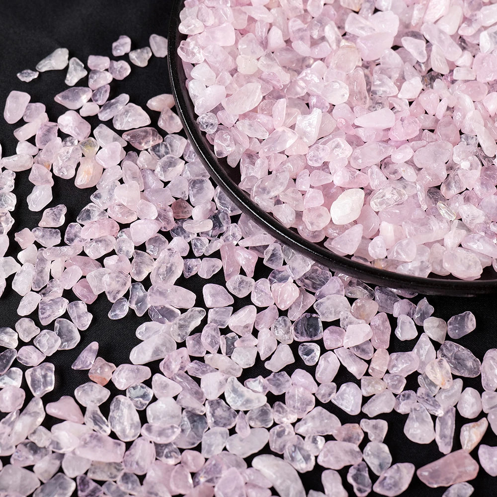 Pink rose quartz crystal gravel scattered on a dark surface.
