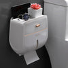Porta papel higiénico blanco con soporte para teléfono negro y un reloj encima.