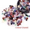 A collection of colorful tumbled crystal stone chips in various shades of purple, green, red, and black.