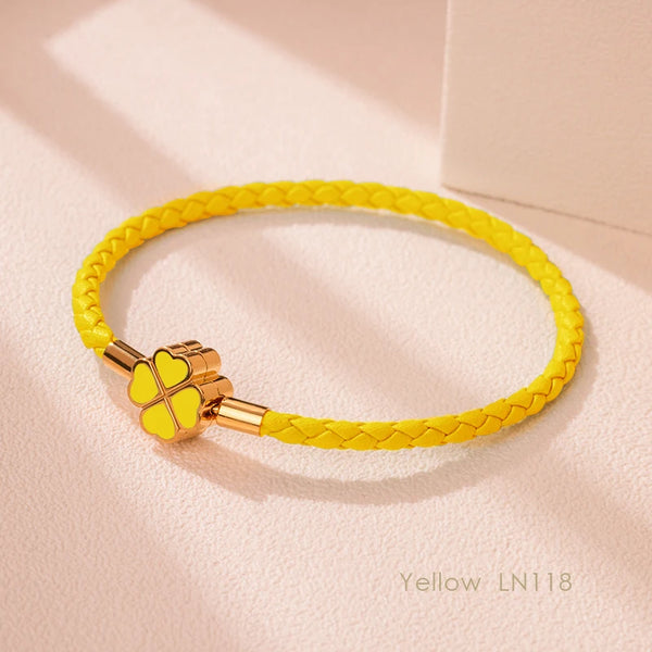 Yellow braided leather bracelet with a gold clasp resting on a light pink surface.