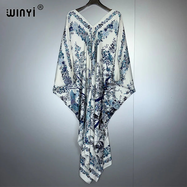 Weißes Maxi-Kleid mit blauem Blumenmuster und botanischen Motiven, auf einem Bügel.