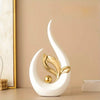 A white ceramic sculpture shaped like a stylized leaf or flame, with a gold accent, displayed on a light surface.
