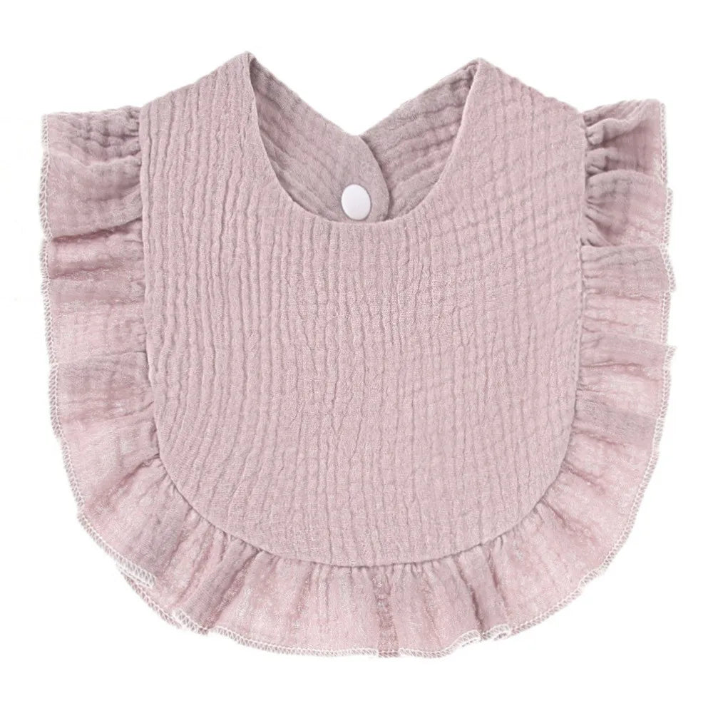 A light pink, textured cotton baby bib in a bandana style with ruffled edges and a small button closure.
