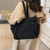A woman is holding a black corduroy tote bag with an adjustable strap against a light beige coat.