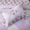 A close-up of a lavender and pink floral patchwork quilt featuring quilted fabric and embroidery.