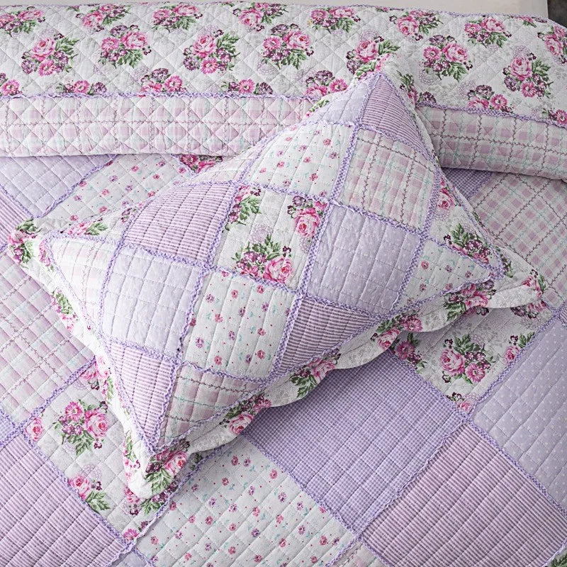 A close-up of a lavender and pink floral patchwork quilt featuring quilted fabric and embroidery.