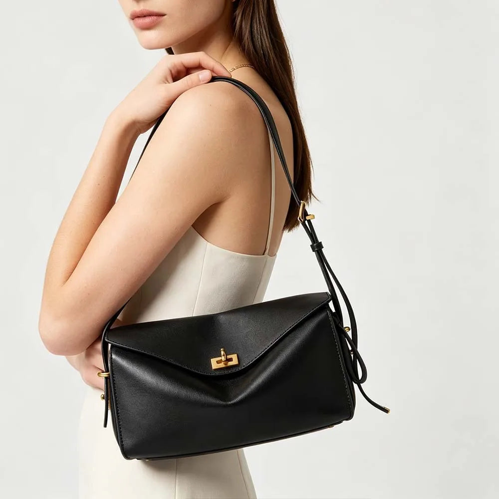 A woman holds a black genuine leather square crossbody bag with a gold lock against a light background.
