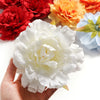 A hand holds a white silk peony flower head surrounded by various colored artificial flowers.