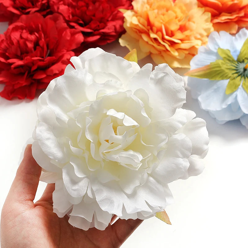 A hand holds a white silk peony flower head surrounded by various colored artificial flowers.