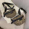Leopardenmuster-Crossbodytasche mit schwarzen Riemen auf hellem grauem Stoff.