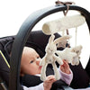 A baby is looking at a soft plush bunny rattle toy hanging from a black stroller or crib frame.