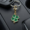 A gold-toned four-leaf clover charm attached to a keychain ring, resting on a black surface.