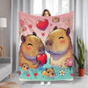 A pink flannel throw blanket featuring a cartoon illustration of two cute, fluffy capybaras swimming in blue water.
